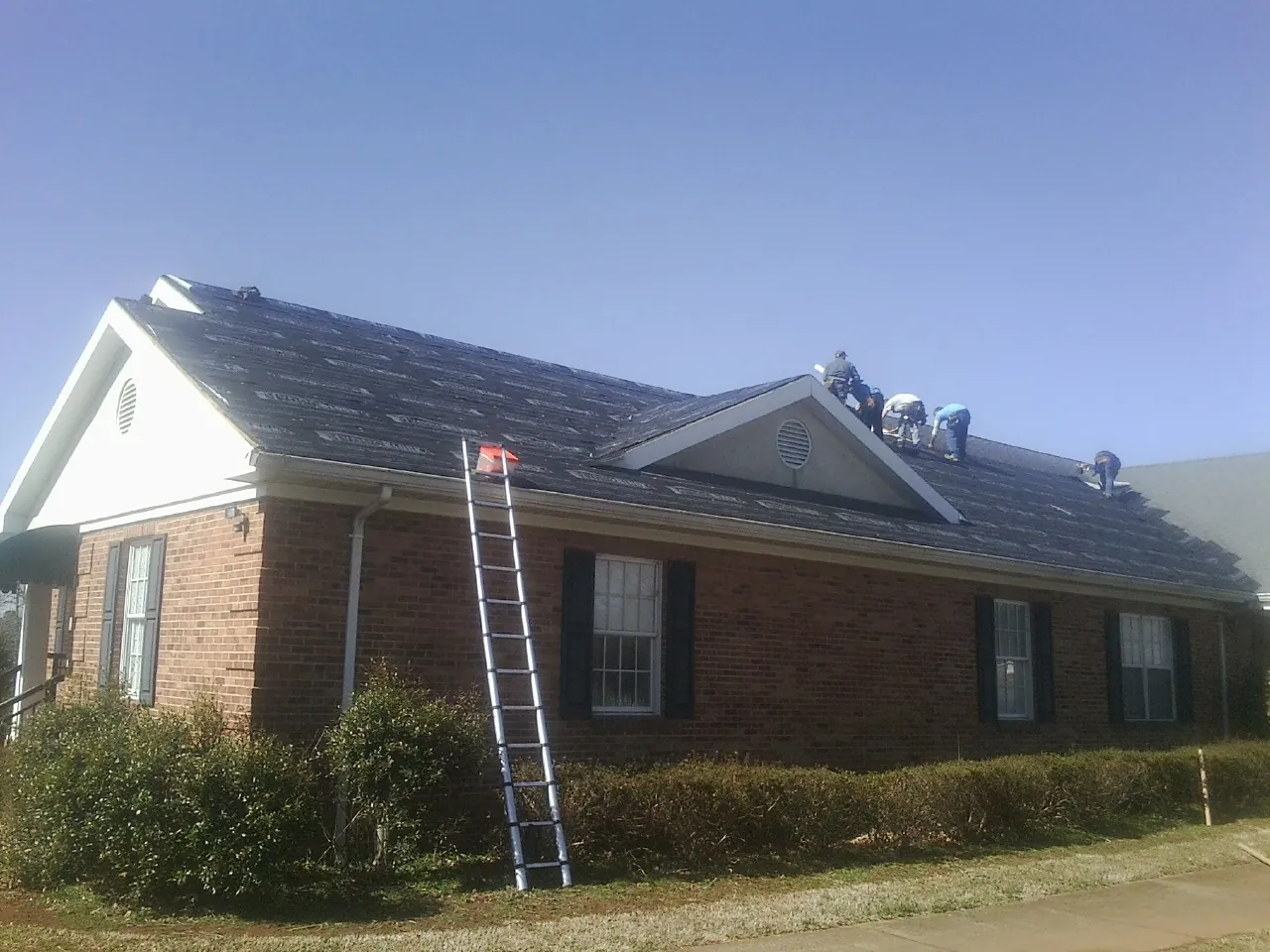 Crew tearing shingles off a brick ranch roof with a ladder set — Emergency Roof Repair work by our crew in Peotone