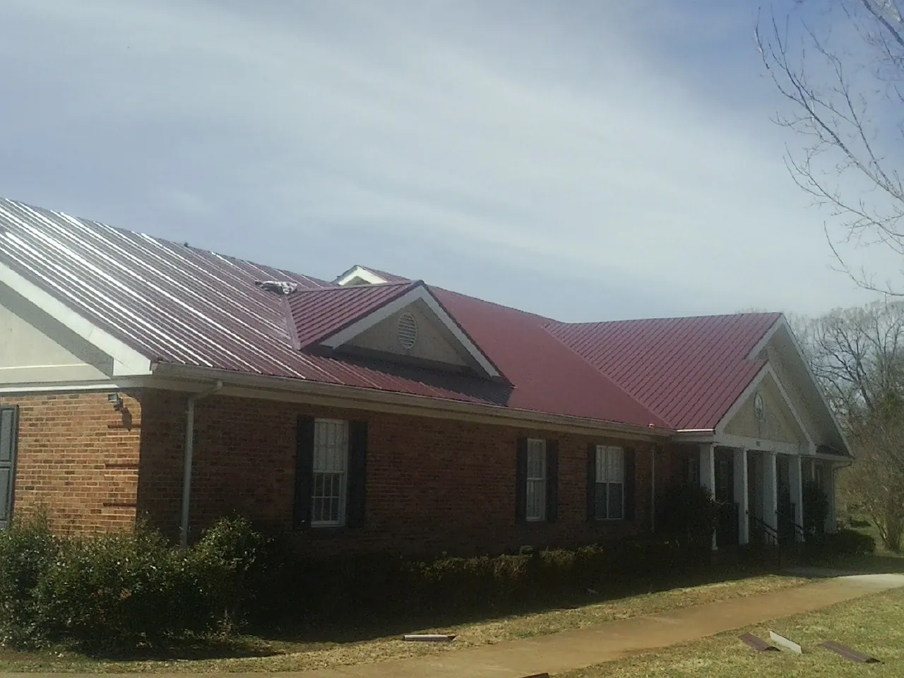 Red metal roof with gabled entries on a long brick building, from a Hail Damage Roof Repair job in Peotone