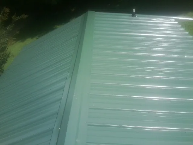 New green metal panels meeting at the ridge of a roof — Flat Roof Repair work by our crew in Peotone