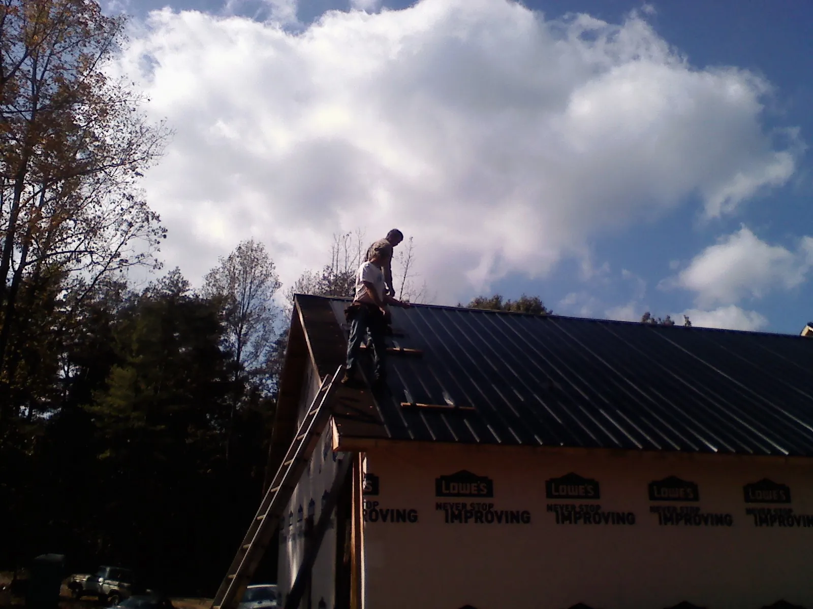 Roofer fastening dark metal panels high against a cloudy sky, from a Roof Inspection job in Peotone
