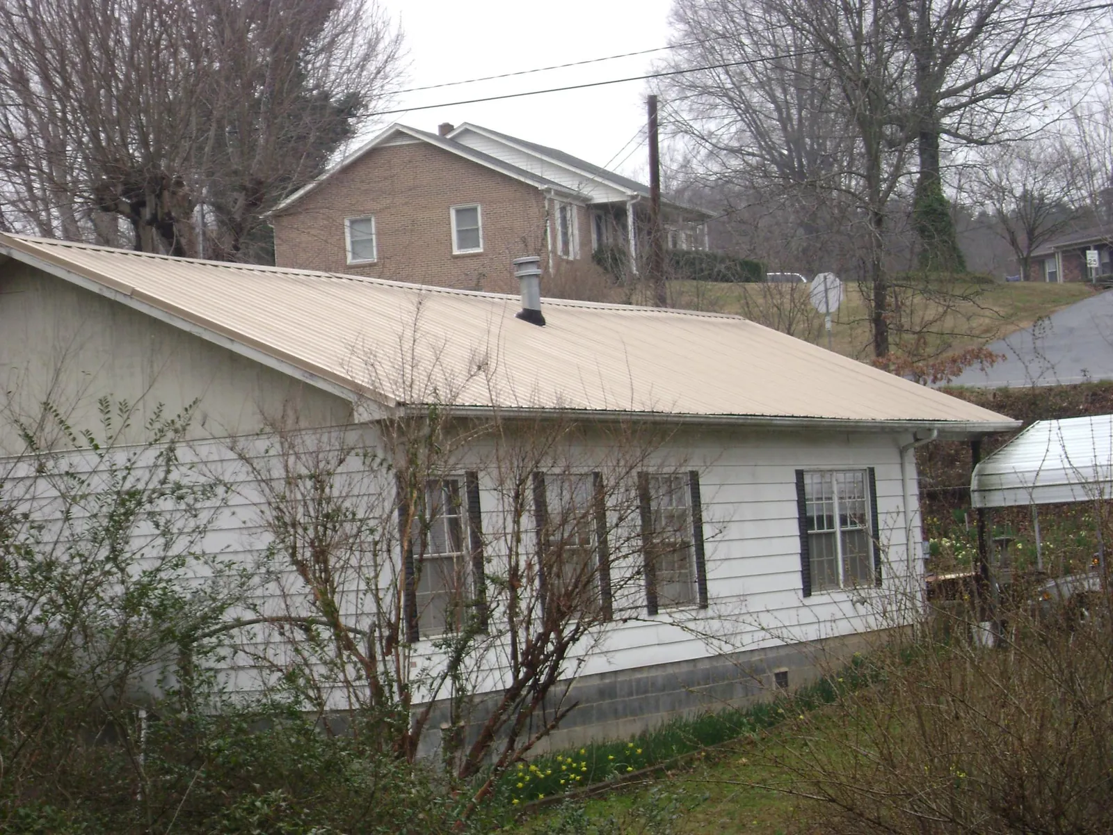 Tan metal roof on a white sided house set into a hillside — Commercial Roofing by Roofing Brothers in Peotone